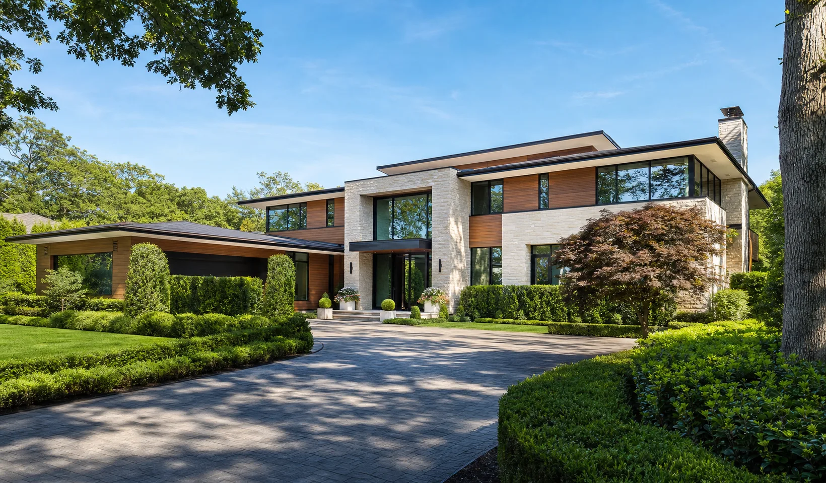 Contemporary North Shore Long Island luxury estate home with stone and cedar siding and expansive glass, photographed in bright daylight, built by Pinnacle Builders LI